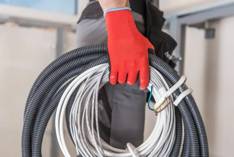 Elektricien met rode werkhandschoen draagt rollen kabel en flexibele installatiebuis