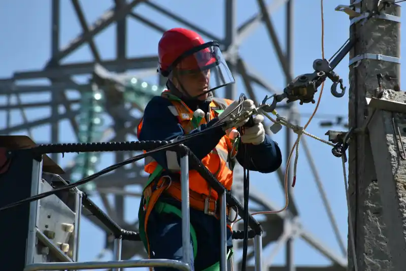 Monteur met helm en gezichtsscherm werkt vanuit een hoogwerker aan een elektriciteitsmast